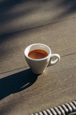Masada beyaz bir fincan espresso kahvesi var. Güneş ışığı. Kadehteki gölge.