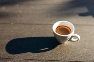 Masanın üzerinde beyaz kahve fincanı var. Güneş ışığı. Kadehteki gölge.