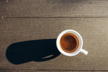 Masanın üzerinde beyaz kahve fincanı var. Güneş ışığı. Kadehteki gölge.