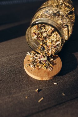 Bitki çayı. Kurutulmuş bitkiler. Cam bir kavanozun yanında çeşitli kurutulmuş bitkiler ve hafif bir arka planda isilikler.