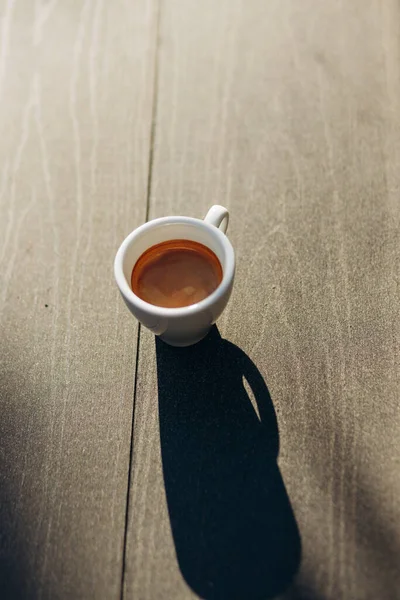 Masada beyaz bir fincan espresso kahvesi var. Güneş ışığı. Kadehteki gölge.