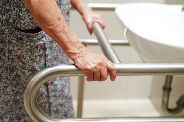 Asyalı yaşlı kadın hasta tuvalette tuvalet desteğini, tırabzan emniyet çubuğunu, hemşire hastanesinde güvenliği kullanıyor..