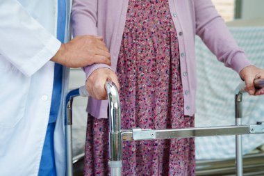 Doktor, Asyalı yaşlı kadın engelli hastaya hemşirelik hastanesinde Walker 'la birlikte yürümesi için yardım ediyor..