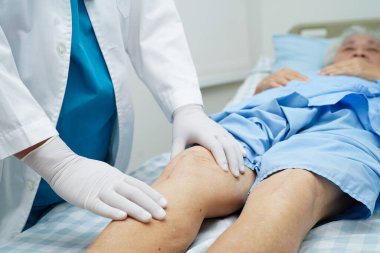 Doktor, hastanede dizinde yara izi olan Asyalı yaşlı kadın hastayı kontrol ediyor..