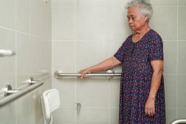 Asyalı yaşlı kadın hasta tuvalette tuvalet desteğini, tırabzan emniyet çubuğunu, hemşire hastanesinde güvenliği kullanıyor..