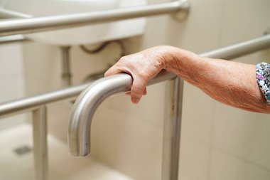 Asyalı yaşlı kadın hasta tuvalette tuvalet desteğini, tırabzan emniyet çubuğunu, hemşire hastanesinde güvenliği kullanıyor..