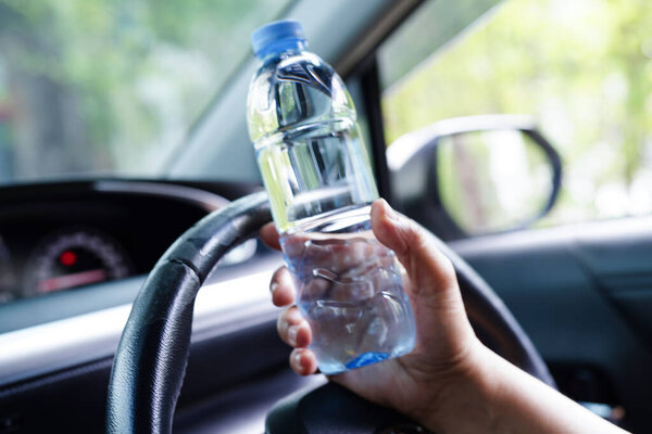Азиатская женщина водитель держит холодную воду для питья в машине, опасно и риск аварии.
