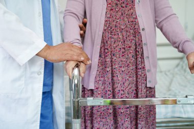 Doktor, Asyalı yaşlı kadın engelli hastaya hemşirelik hastanesinde Walker 'la birlikte yürümesi için yardım ediyor..