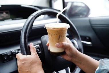 Asyalı kadın sürücü arabada buzlu kahve bardağı tutuyor, tehlikeli ve kaza riski var.