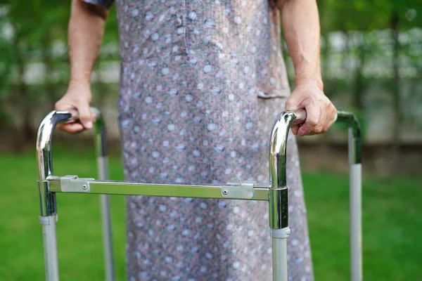 Asian elderly woman disability patient walk with walker in park, medical concept.