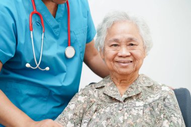 Doktor, hastanede tekerlekli sandalyede oturan Asyalı yaşlı kadın engelli hastaya yardım ediyor..