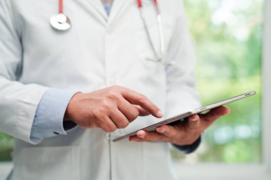 Asyalı doktor hasta raporlarını okumak için tablet bilgisayar kullanıyor. Hastanedeki sağlık sorunlarını internette araştırıyor ve kontrol ediyor..