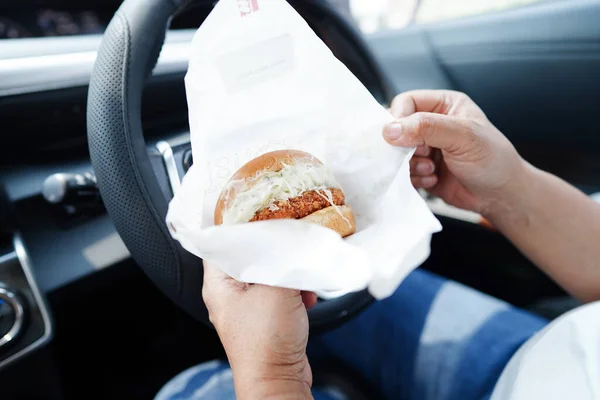 Asian woman driver hold and eat hamburger in car, dangerous and risk an accident.