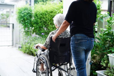 Bakıcı, hastanede tekerlekli sandalyede oturan Asyalı yaşlı kadın maluliyet hastasına yardım ediyor..
