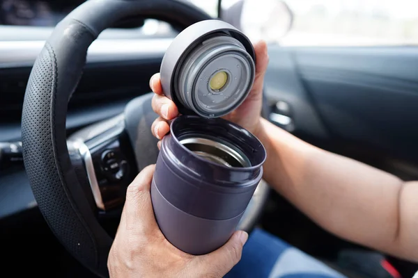 stock image Asian woman driver hold thermo mug with hot coffee in car, dangerous and risk an accident.