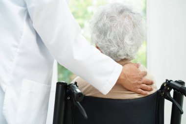 Doktor, hastanede tekerlekli sandalyede oturan Asyalı yaşlı kadın engelli hastaya yardım ediyor..