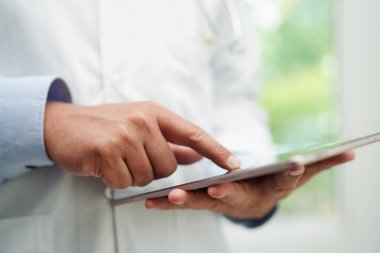 Asyalı doktor hasta raporlarını okumak için tablet bilgisayar kullanıyor. Hastanedeki sağlık sorunlarını internette araştırıyor ve kontrol ediyor..