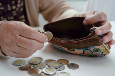 Retired elderly woman counting coins money and worry about monthly expenses and treatment fee payment.