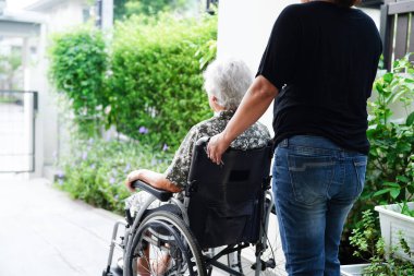 Bakıcı, hastanede tekerlekli sandalyede oturan Asyalı yaşlı kadın maluliyet hastasına yardım ediyor..