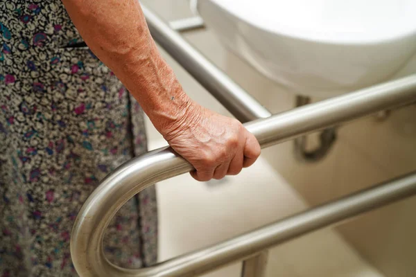 Asian elderly old woman patient use toilet support rail in bathroom, handrail safety grab bar, security in nursing hospital.
