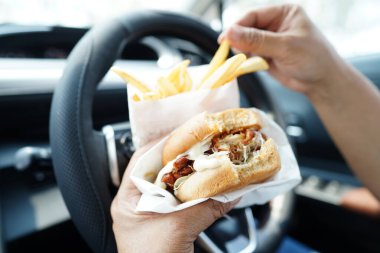 Asyalı kadın sürücü arabada patates kızartması yer ve tutar. Tehlikeli ve kaza riski taşır..