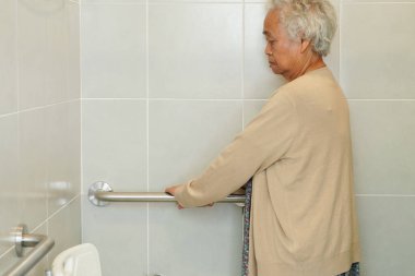 Asyalı yaşlı kadın hasta tuvalette tuvalet desteğini, tırabzan emniyet çubuğunu, hemşire hastanesinde güvenliği kullanıyor..