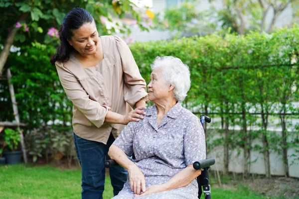 stock image Caregiver help Asian elderly woman disability patient sitting on wheelchair in park, medical concept.