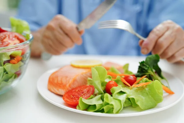 アジアの高齢女性患者は病院で健康食品のためのサーモンの杭と野菜のサラダを食べる — ストック写真