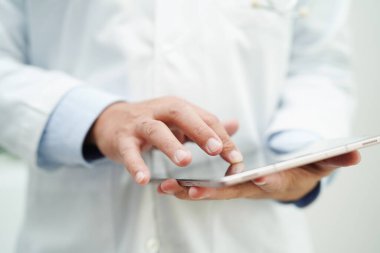 Asyalı doktor hasta raporlarını okumak için tablet bilgisayar kullanıyor. Hastanedeki sağlık sorunlarını internette araştırıyor ve kontrol ediyor..