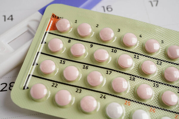 Pregnancy test with birth control pills and condom for female on calendar, ovulation day.