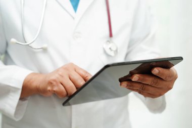 Hastanedeki hastaları arama yöntemi için cep telefonu ya da tablet tutan Asyalı kadın doktor.