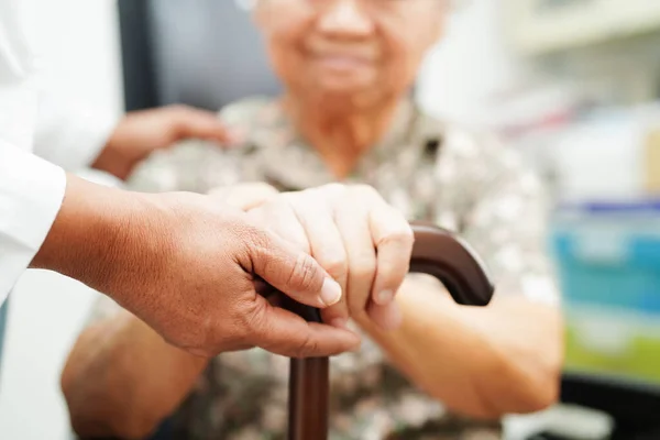 Stock image Doctor help Asian elderly disability woman patient holding walking stick in wrinkled hand at hospital.