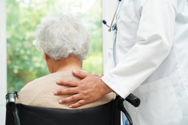 Doktor, hastanede tekerlekli sandalyede oturan Asyalı yaşlı kadın engelli hastaya yardım ediyor..