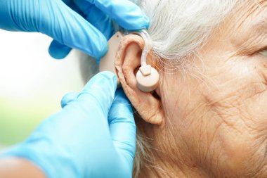 Doktor işitme kaybını azaltmak için yaşlı hasta kulağına işitme cihazı takıyor..