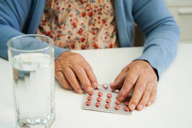 Elinde bardakta su olan hap tutan Asyalı yaşlı bir kadın. Güçlü, sağlıklı bir tıbbi konsept.. 