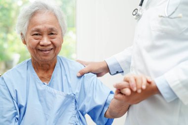 Doktor, hastanede tekerlekli sandalyede oturan Asyalı yaşlı kadın engelli hastaya yardım ediyor..