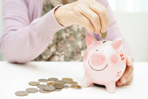 Retired elderly woman putting coins money in piggy bank and worry about monthly expenses and treatment fee payment.