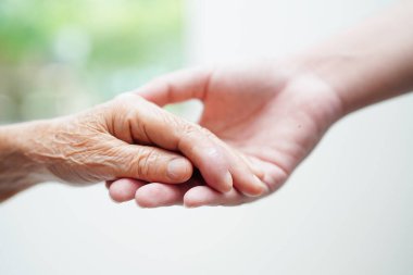 Asyalı genç bir çocuk yaşlı büyükanneyi sevgi ve özenle bir arada tutuyor..