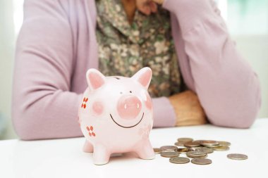 Emekli yaşlı kadın domuz kumbarasıyla bozuk para sayıyor ve aylık giderleri ve tedavi ücretini düşünüyor..