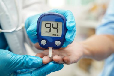 Diyabet tedavisinde kan şekeri seviyesini kontrol etmek için dijital glikoz ölçer kullanan Asyalı doktor.