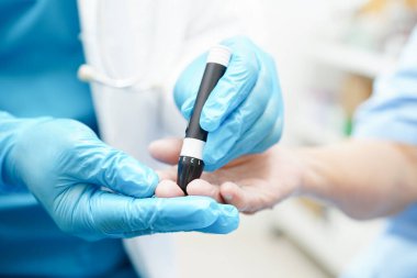 Asyalı doktor, kıdemli hasta parmağındaki tükenmez kalemle şeker seviyesini diyabet tedavisinde kontrol ediyor..
