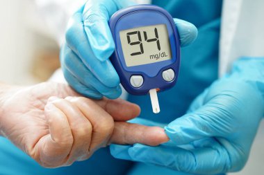 Asyalı doktor, kıdemli hasta parmağındaki tükenmez kalemle şeker seviyesini diyabet tedavisinde kontrol ediyor..