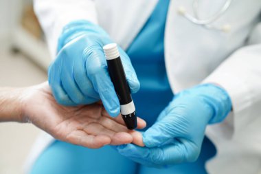 Asyalı doktor, kıdemli hasta parmağındaki tükenmez kalemle şeker seviyesini diyabet tedavisinde kontrol ediyor..