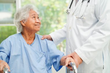 Doktor, Asyalı yaşlı kadın engelli hastaya hemşirelik hastanesinde Walker 'la birlikte yürümesi için yardım ediyor..