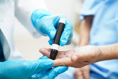 Asyalı doktor, kıdemli hasta parmağındaki tükenmez kalemle şeker seviyesini diyabet tedavisinde kontrol ediyor..