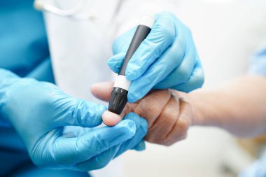 Asyalı doktor, kıdemli hasta parmağındaki tükenmez kalemle şeker seviyesini diyabet tedavisinde kontrol ediyor..