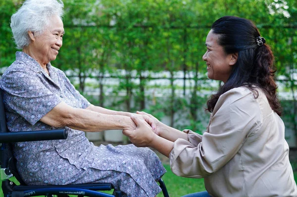 Stock image Caregiver help Asian elderly woman disability patient sitting on wheelchair in park, medical concept.