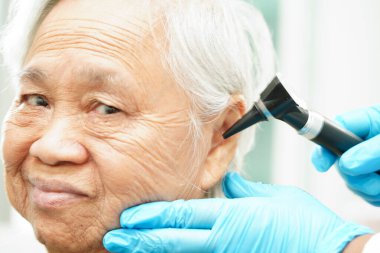 Otolaryngologist ya da ENT hekim doktoru yaşlı hasta kulağını otoskopla muayene ediyor, işitme sorunu var.. 