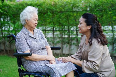 Doktor, parkta tekerlekli sandalyede oturan Asyalı yaşlı kadın engelli hastaya yardım ediyor. Tıbbi konsept..