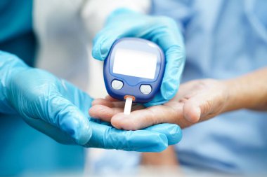 Diyabet tedavisinde kan şekeri seviyesini kontrol etmek için dijital glikoz ölçer kullanan Asyalı doktor.